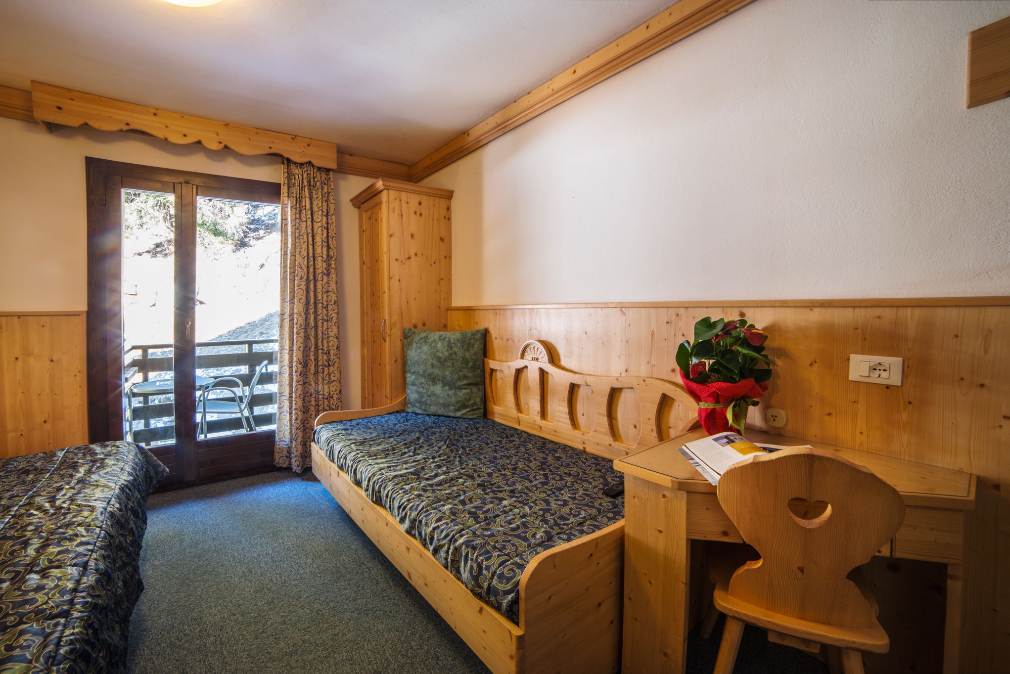 A wooden room with two single beds, a wooden desk, and a chair.