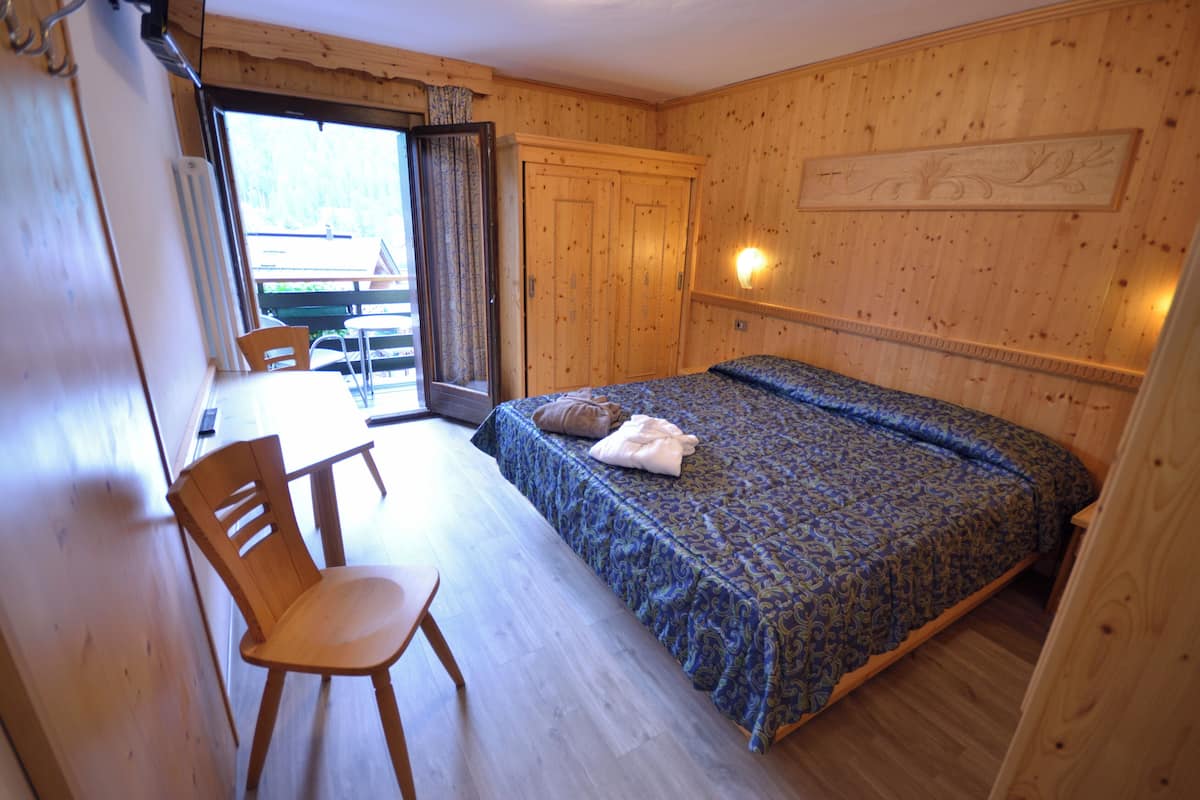 Un dormitorio con cama, una silla de madera, una mesa y vistas a través de una puerta.