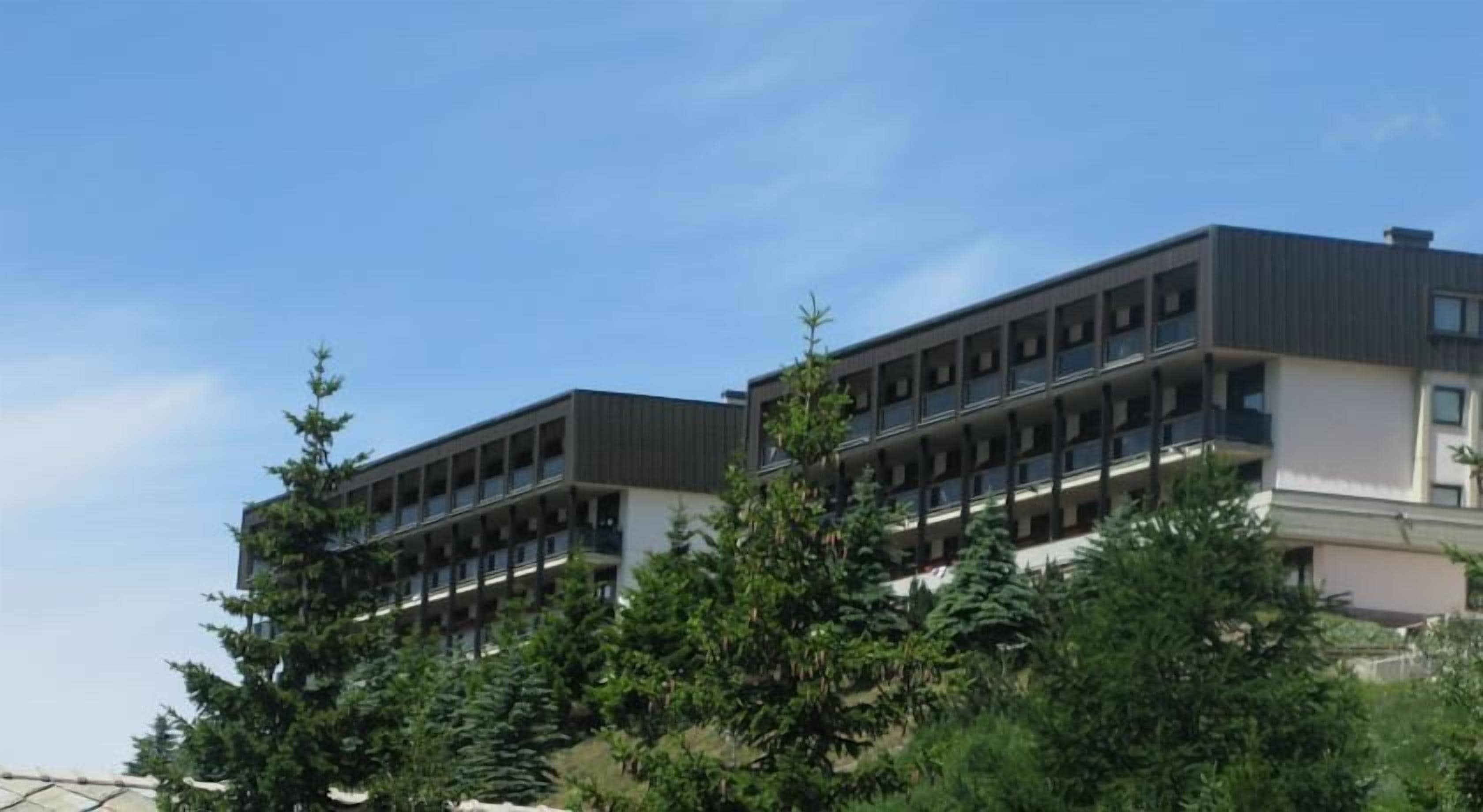 A modern multi-story building with balconies, surrounded by dense greenery.