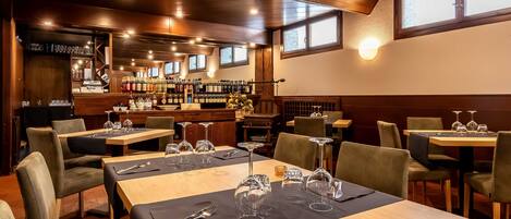 A restaurant with wooden tables, chairs, and a bar area with wine bottles.