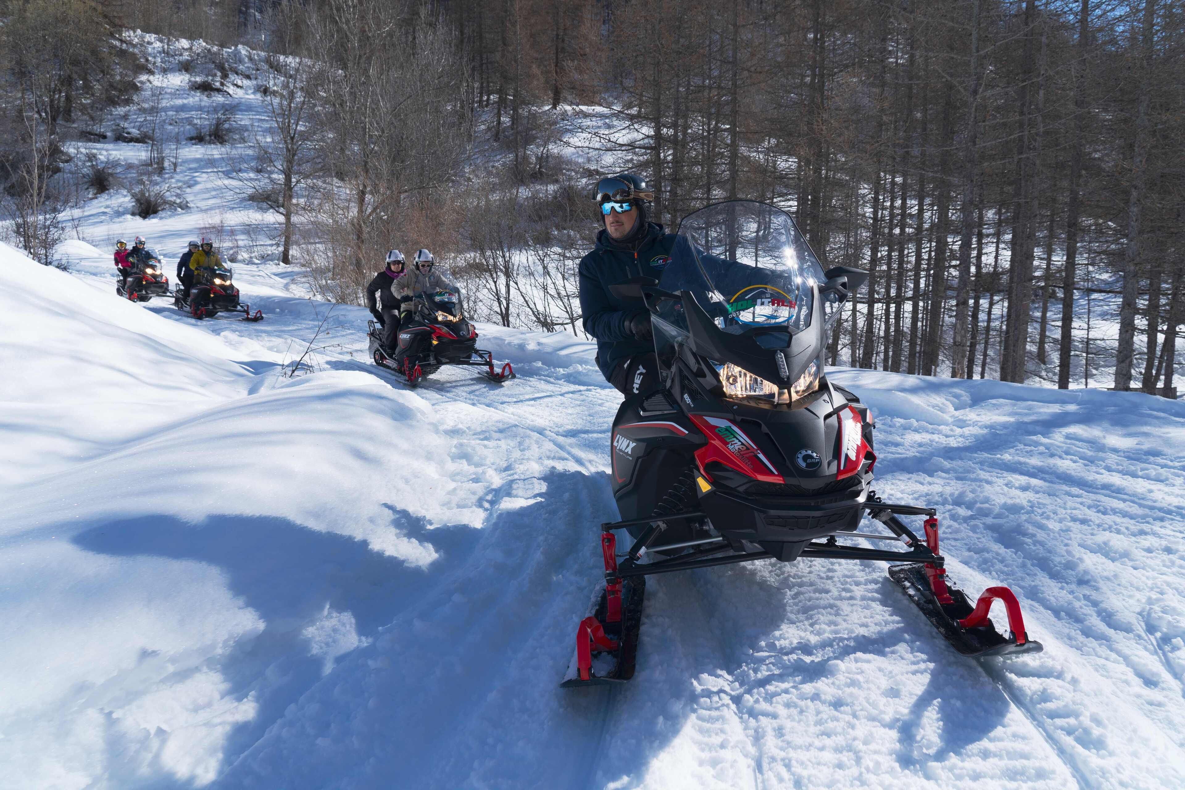 A snowmobile with a rider, surrounded by snow and trees.