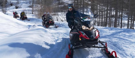 A snowmobile with a rider, surrounded by snow and trees.