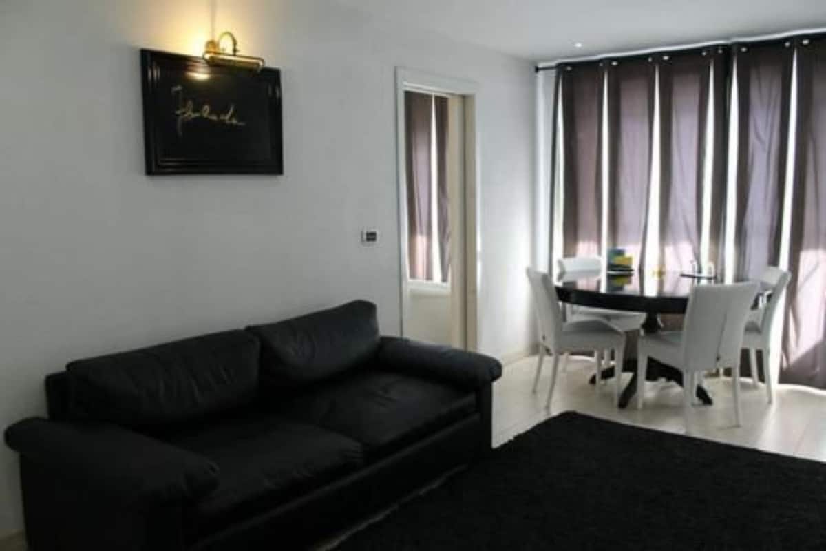 A modern living room with a black leather sofa, a dining table with white chairs, and a black rug.