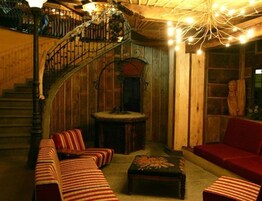 Una stanza accogliente con una scala in legno, un divano rosso e un poggiapiedi decorato.