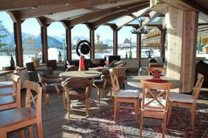 Una terrazza esterna in legno con tavoli e sedie, affacciata su un paesaggio innevato.