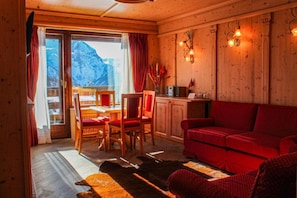 A wooden interior with a dining area, red sofa, and a view of mountains.