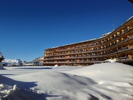 Un hotel a più piani con balconi, terreno innevato e cielo azzurro limpido.