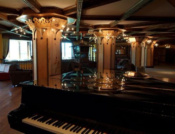 A grand piano in a warmly lit room with ornate columns and a large window.