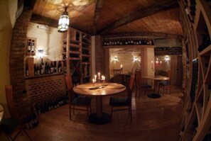 A cozy room with a round table, chairs, a brick wall, and shelves with bottles.