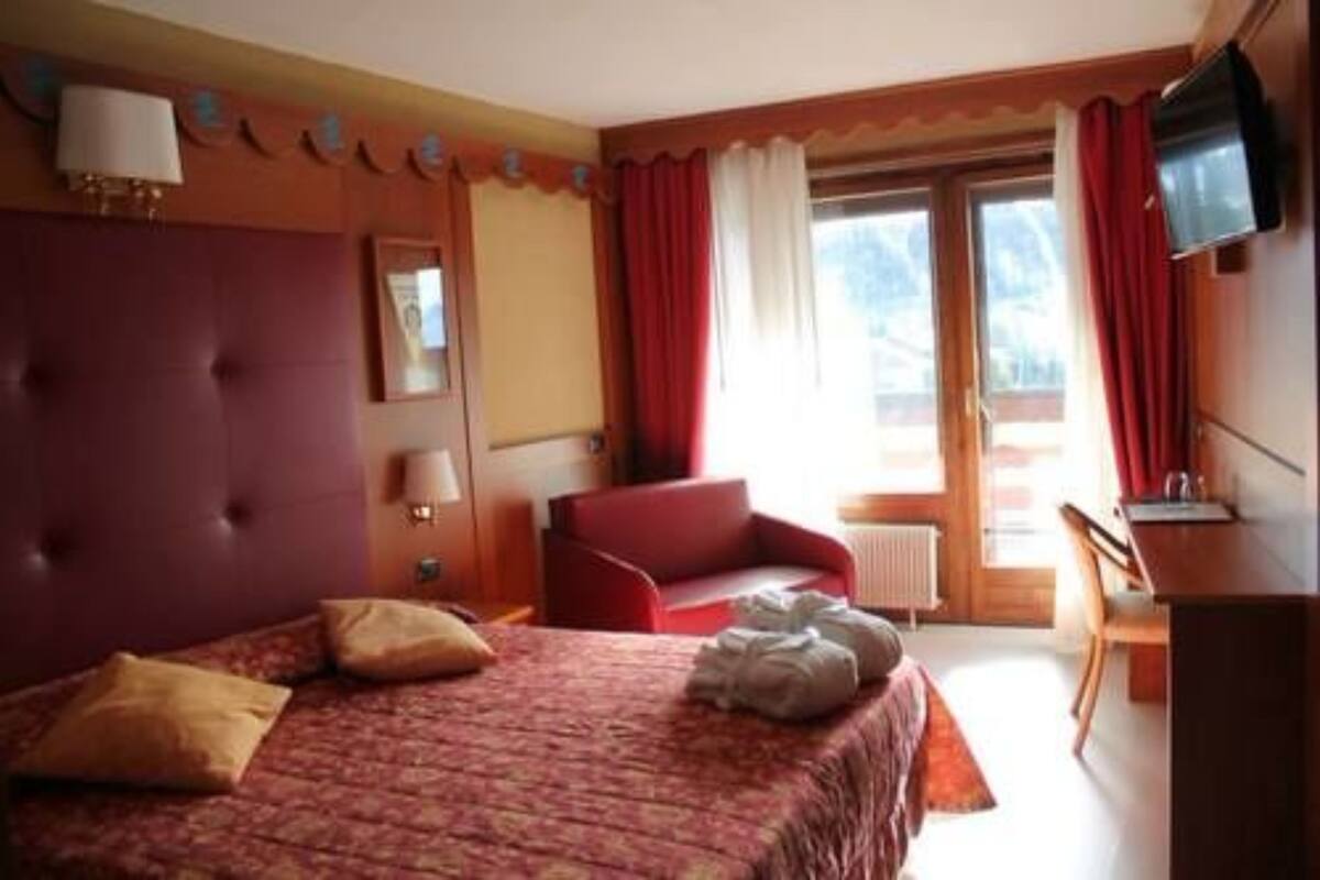 A hotel room with a large bed, a red armchair, a desk, and a television.