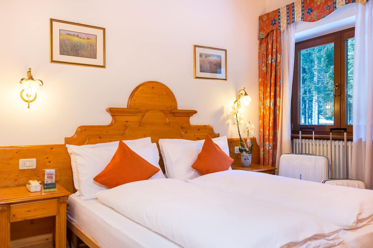 A neatly made bed with white and orange pillows, a wooden headboard, and two framed pictures on the wall.