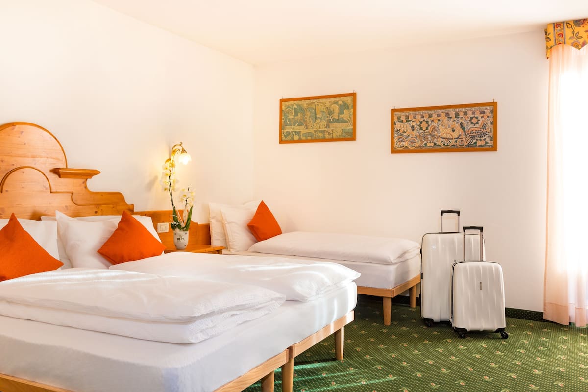 A hotel room with two beds, a wooden headboard, a nightstand with a lamp, a vase with flowers, and a suitcase.