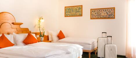 A hotel room with two beds, a wooden headboard, a nightstand with a lamp, a vase with flowers, and a suitcase.