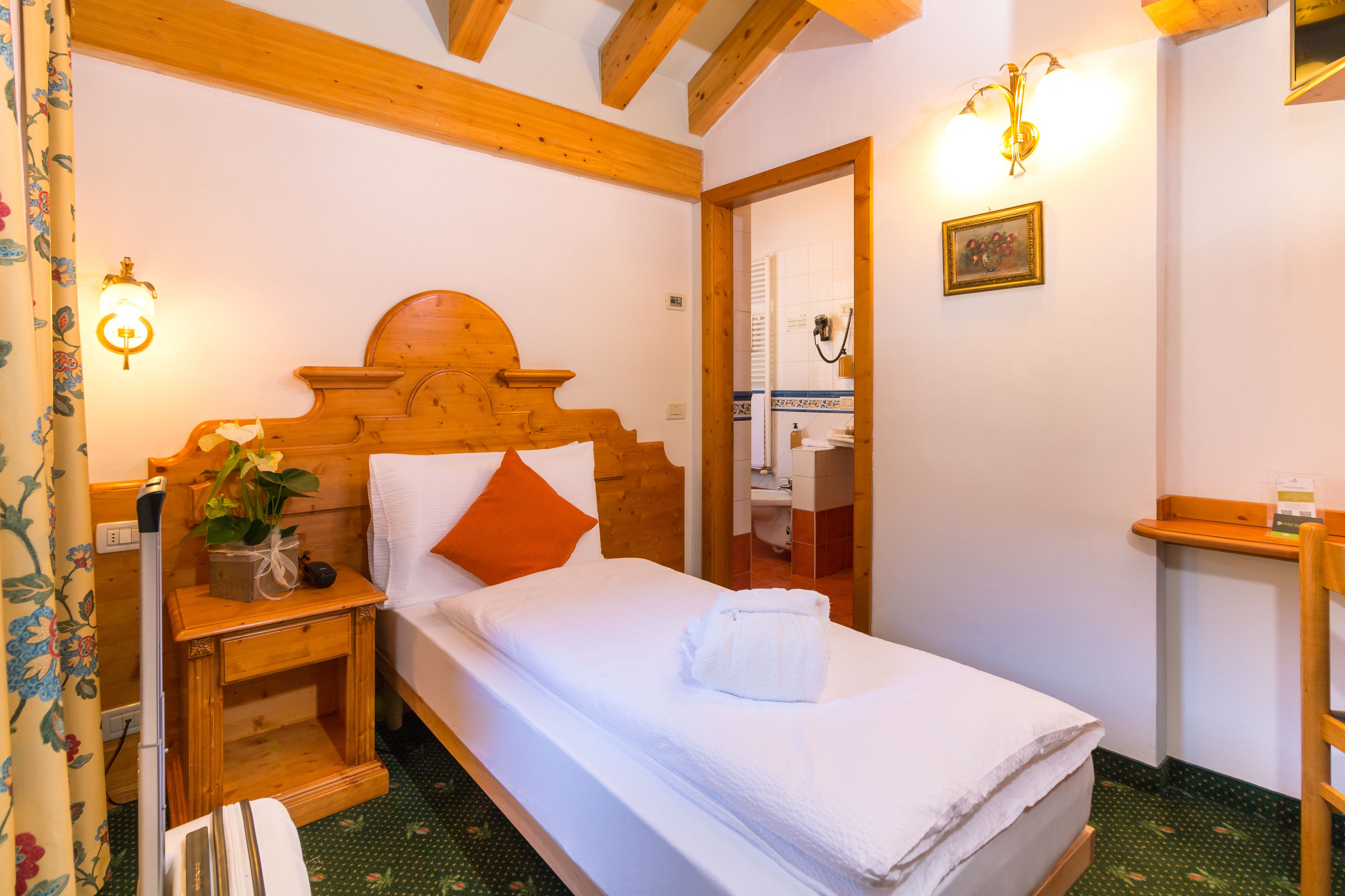 A wooden-framed bed with white bedding and an orange pillow in a room with wooden beams and a mirror.
