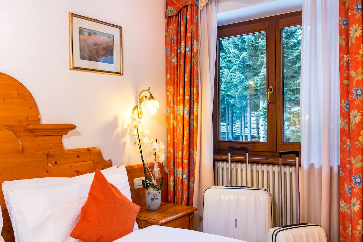 A hotel room with a wooden bed, a white radiator, a window with curtains, and a suitcase.