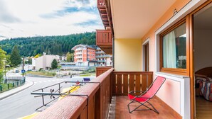 A balcony with a red chair, a view of a road, and a building in the background. - Hotel Bonapace (Pinzolo)
