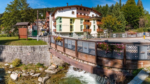 A hotel with a balcony, a stone wall, and a bridge over a flowing river. - Hotel Bonapace (Pinzolo)