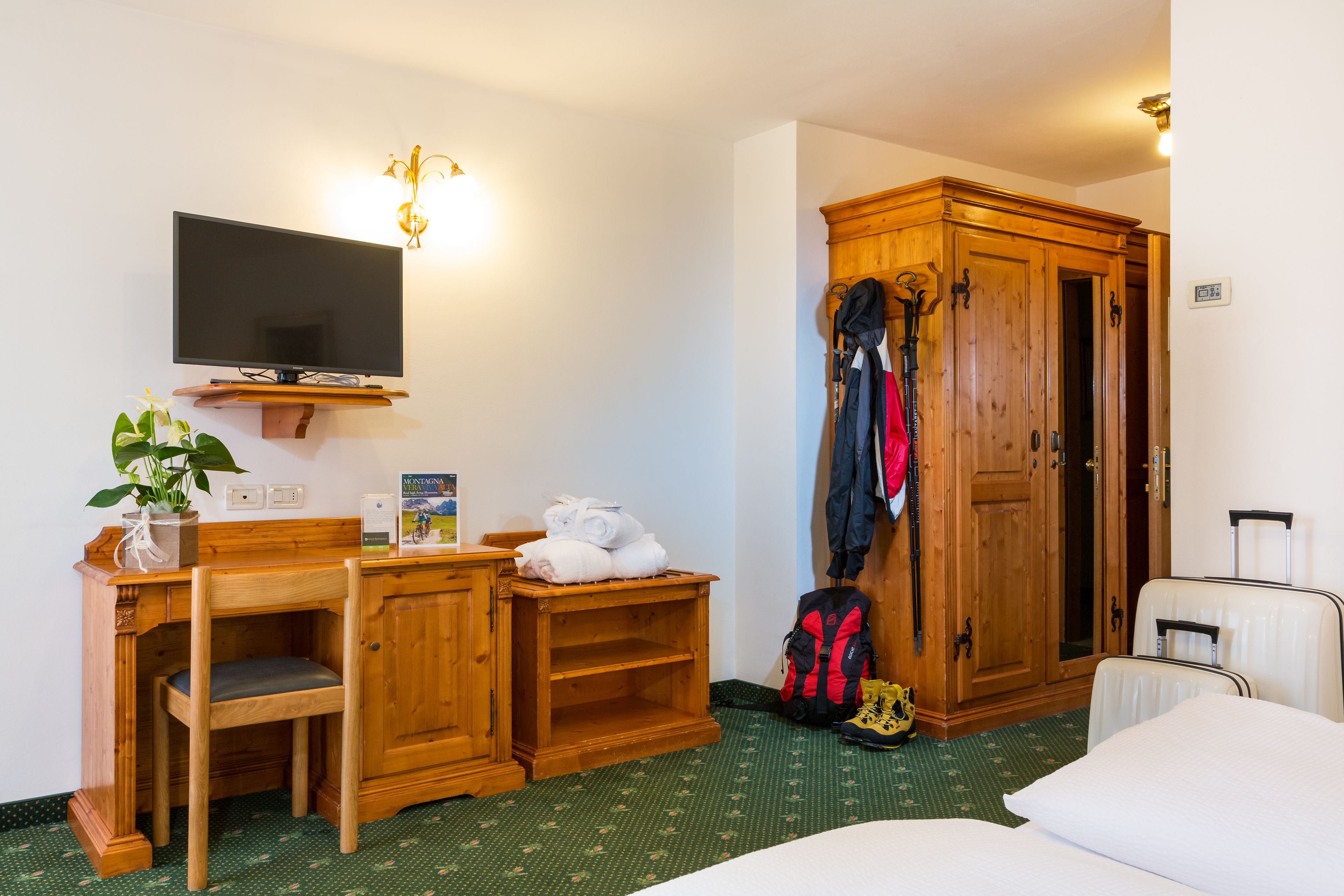 Een hotelkamer met een bed, een bureau met stoel, een televisie, een kledingkast en een kapstok.