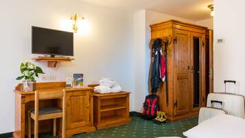Een hotelkamer met een bed, een bureau met stoel, een televisie, een kledingkast en een kapstok.