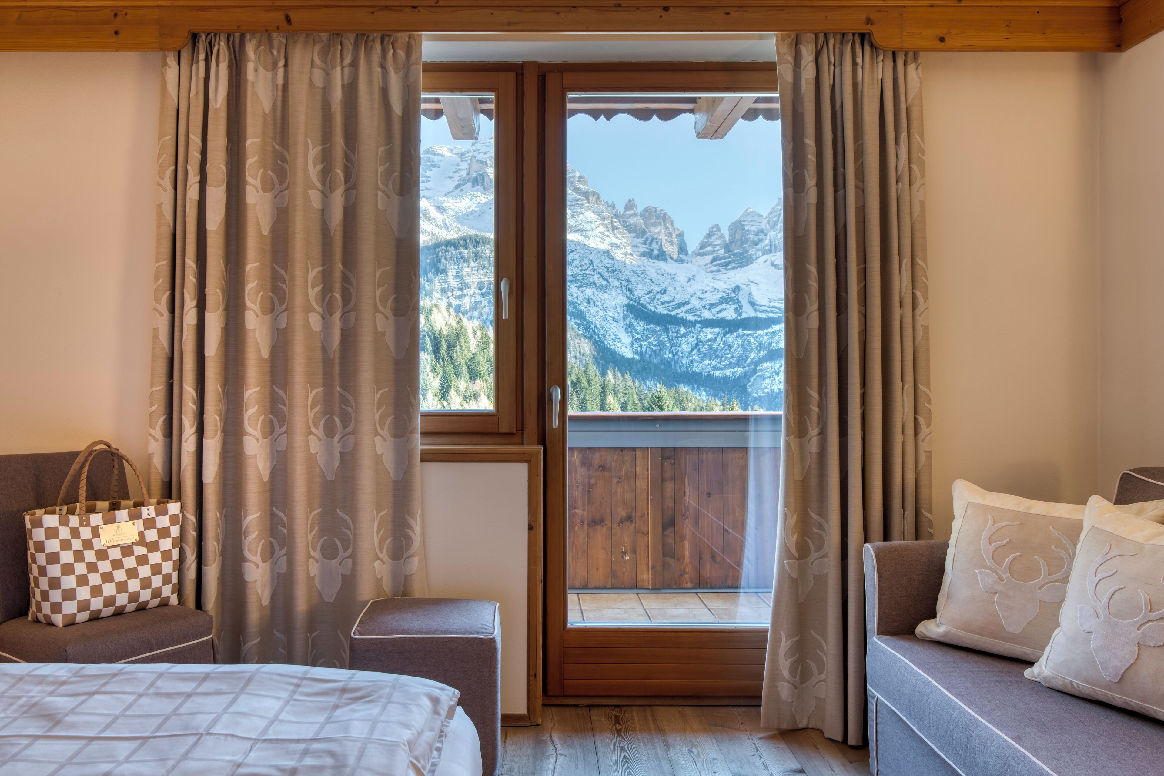 Una stanza con un letto, un divano, una panca di legno e vista sulle montagne attraverso una finestra.