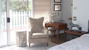 Een kamer met een fauteuil met zebraprint, een eettafel met stoelen, een klein beeldje en een bed met een bloemenbedekking.
