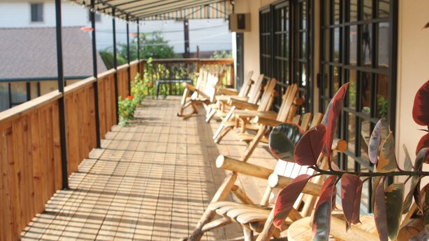 Een overdekt terras met houten stoelen en een betegelde vloer.