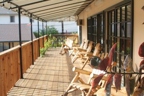 A covered outdoor seating area with wooden chairs and a tiled floor.