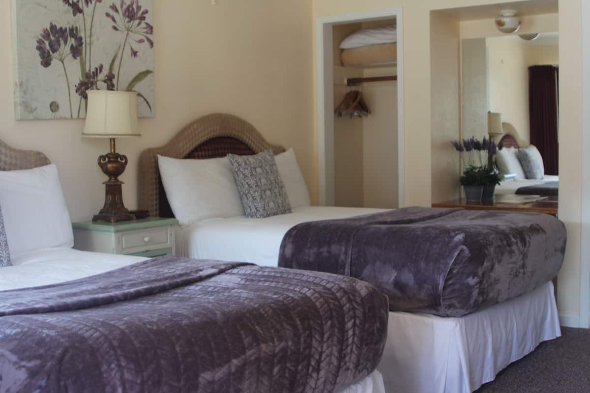 A hotel room with two beds, a nightstand, a lamp, a mirror, and a painting on the wall.