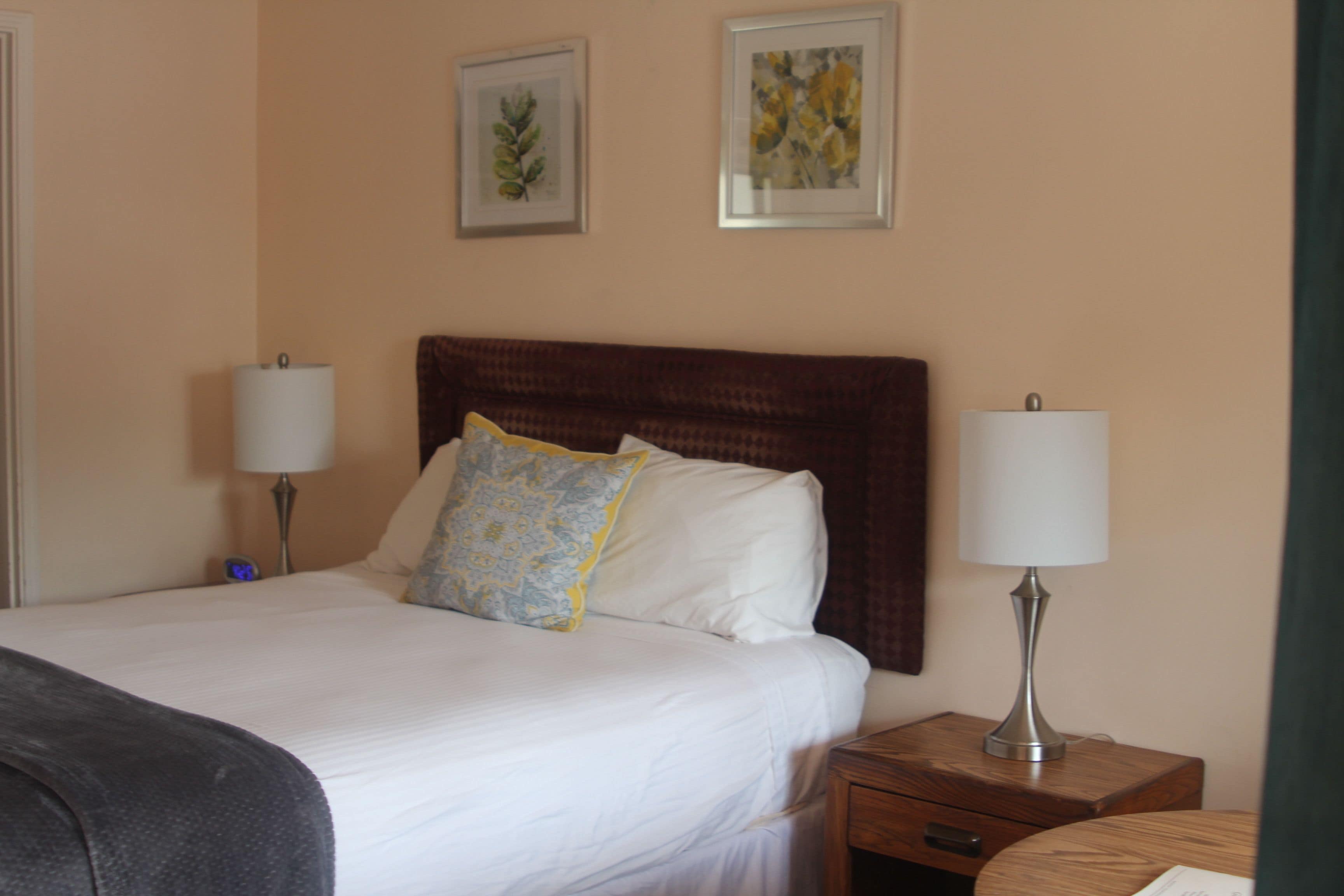 A hotel room with a large bed, two bedside lamps, a wooden nightstand, and two framed pictures on the wall.