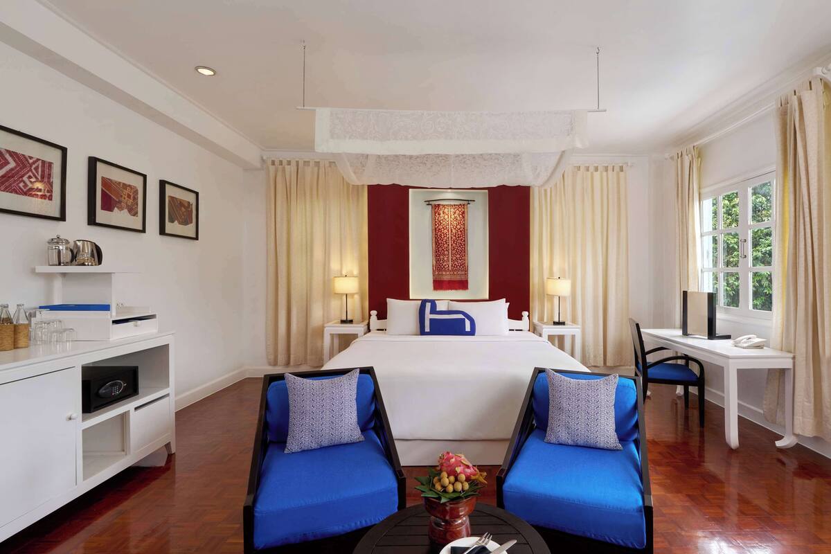 Une chambre d’hôtel avec un grand lit, deux fauteuils bleus, un bureau et une télévision.