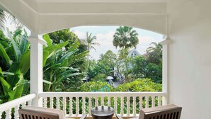 Un balcón con dos sillas de madera y una mesa redonda pequeña, con vistas a un jardín exuberante con diversas plantas y una piscina.