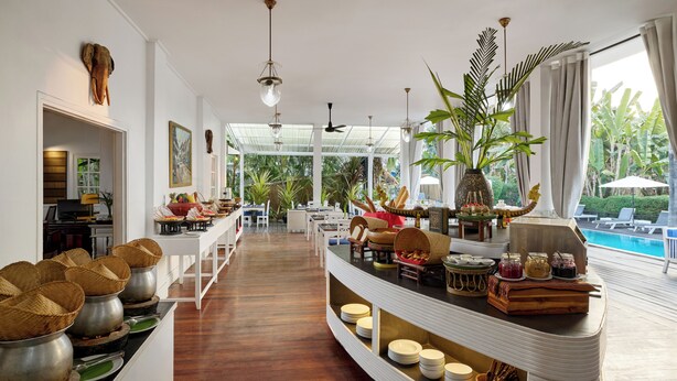 Amplio espacio interior con una larga barra, diferentes alimentos y vistas a una piscina exterior.