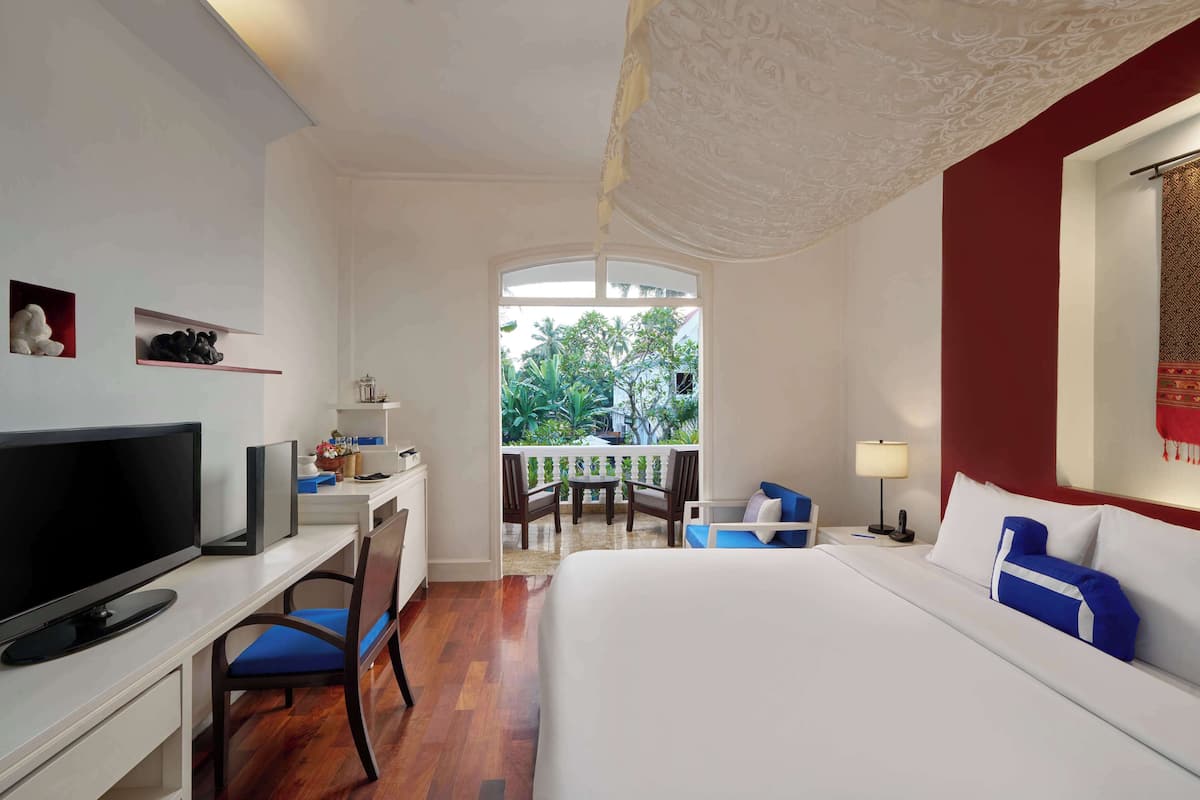 Une chambre d’hôtel comprenant un lit, un bureau avec une télévision, une chaise, un balcon avec une table et des chaises, et une vue sur la verdure environnante.