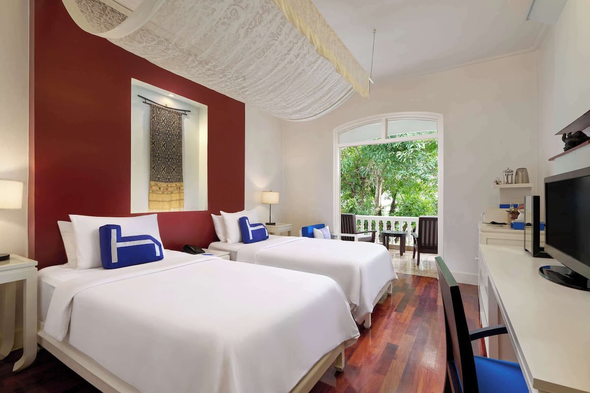 Une chambre d’hôtel avec deux lits, une télévision, un balcon et une vue sur la verdure.