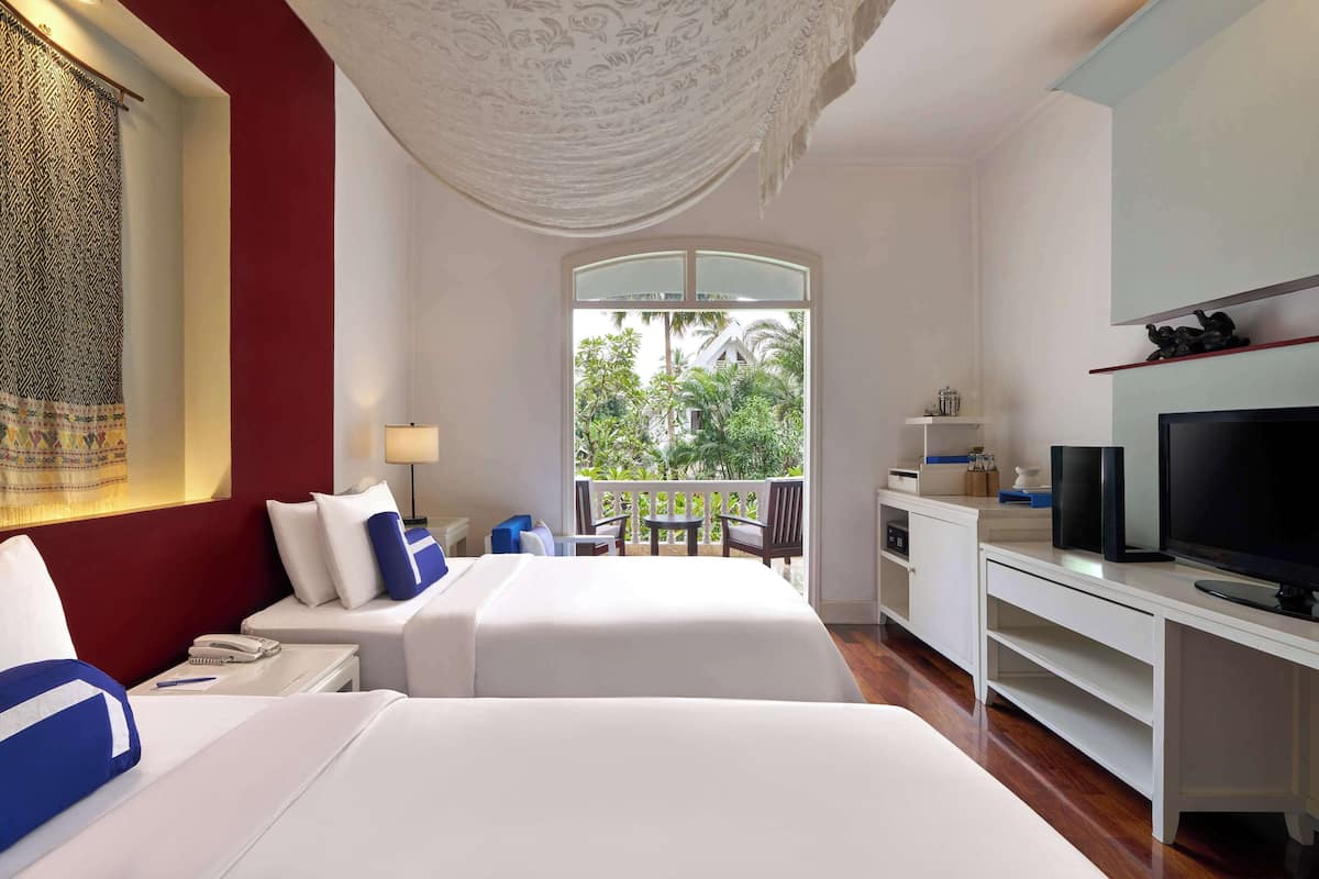 Une chambre d’hôtel avec deux lits, une télévision, un bureau et un balcon donnant sur un espace verdoyant.