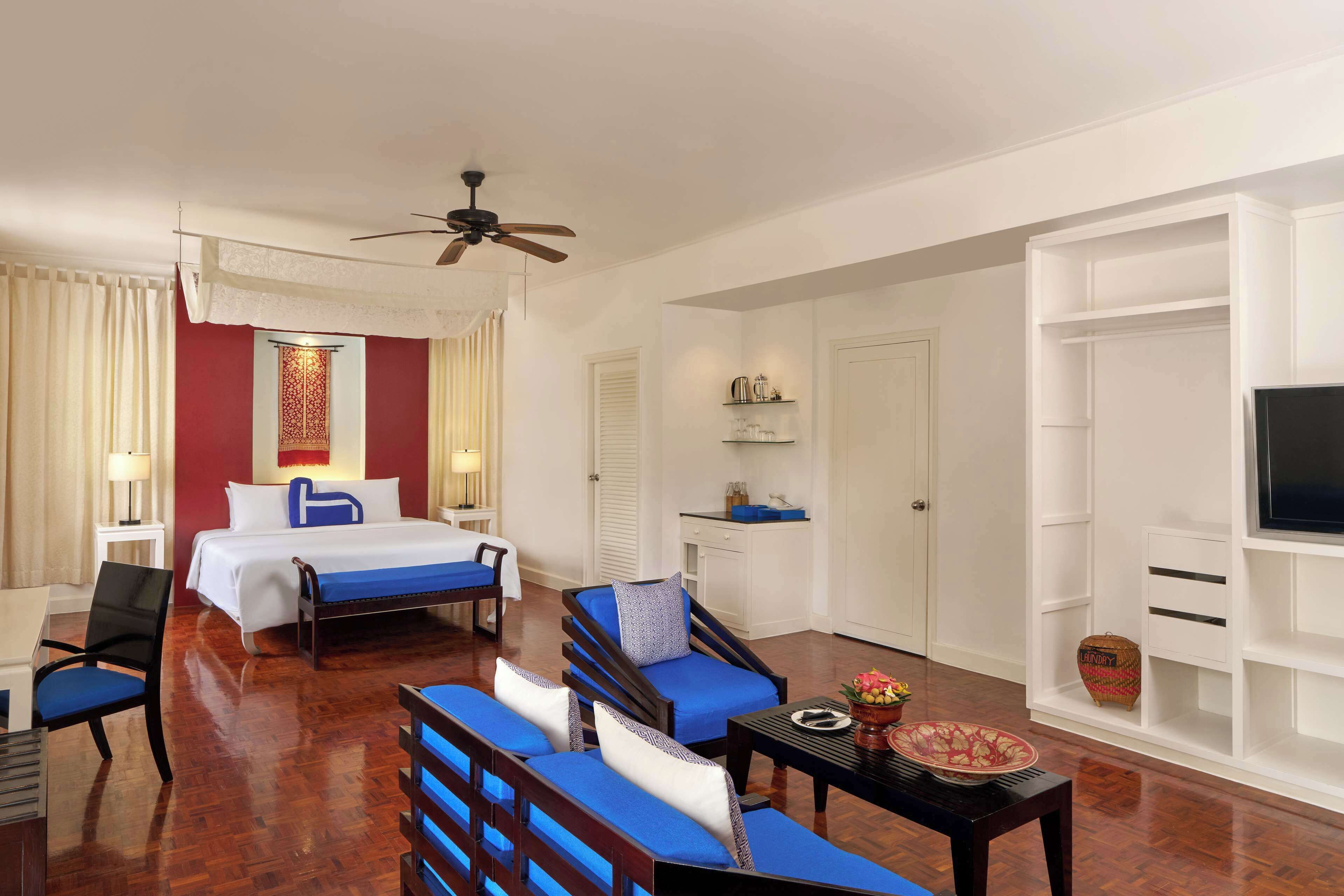 Una habitación de hotel con cama, escritorio, silla, sofá, televisión y ventilador de techo.