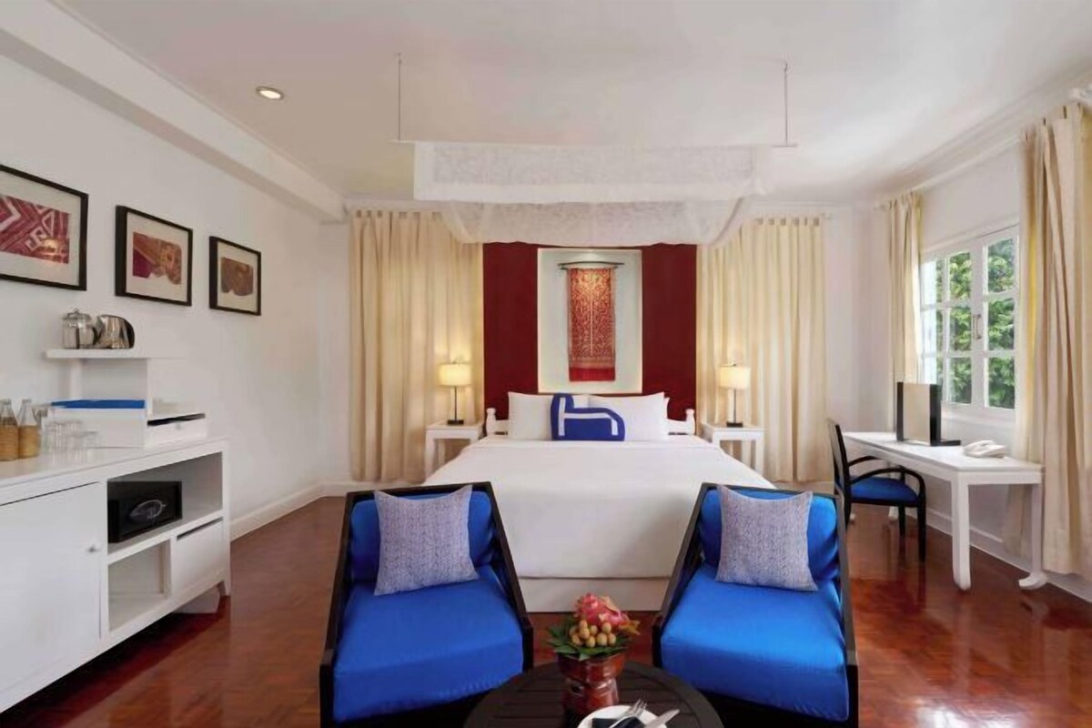 Une chambre d’hôtel avec un grand lit, deux fauteuils bleus, un bureau et une télévision.
