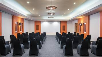 A conference room with rows of black chairs, a projector screen, and three pendant lights.