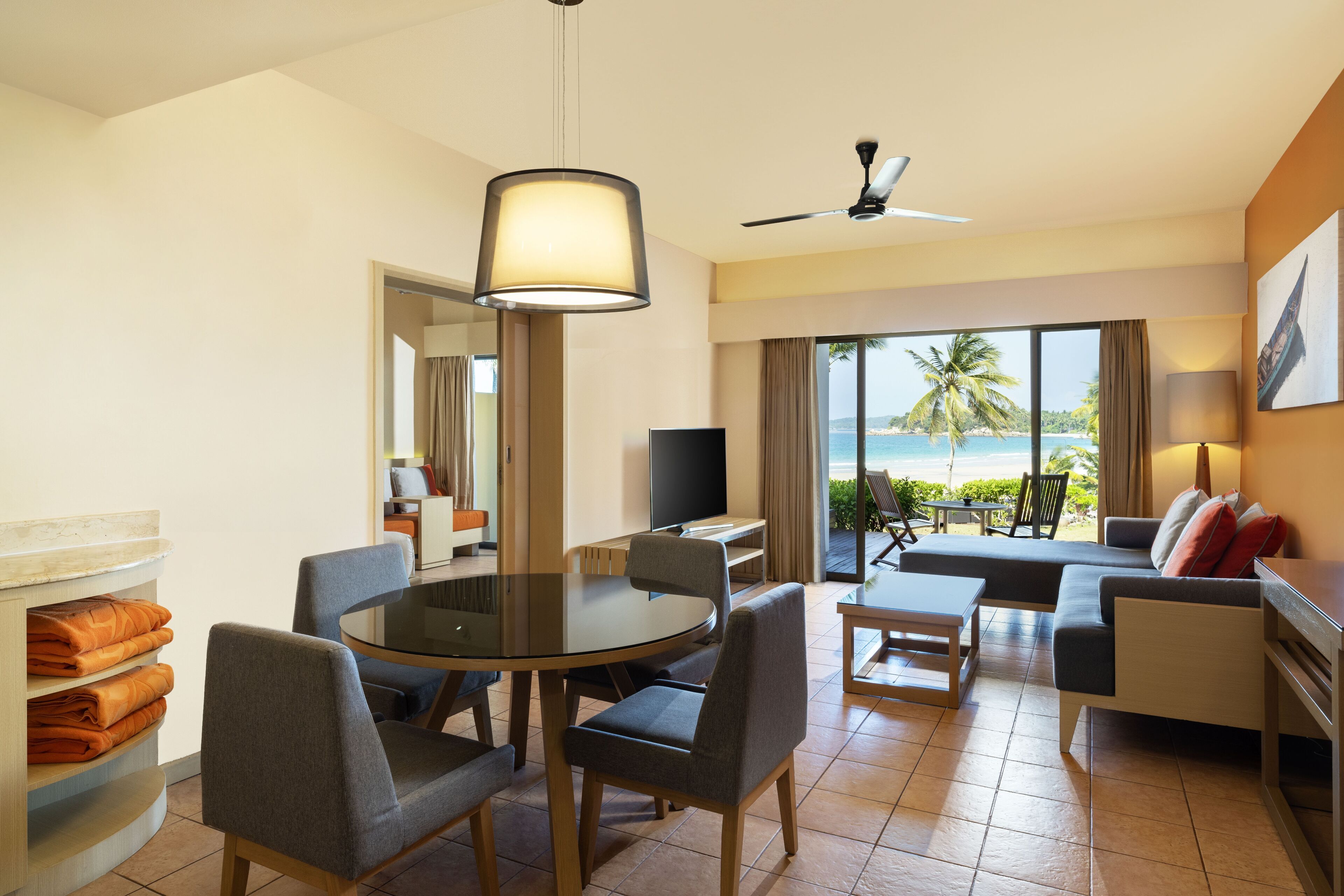 Habitación de hotel con zona de comedor, sofá, televisión y balcón con vista a la playa.
