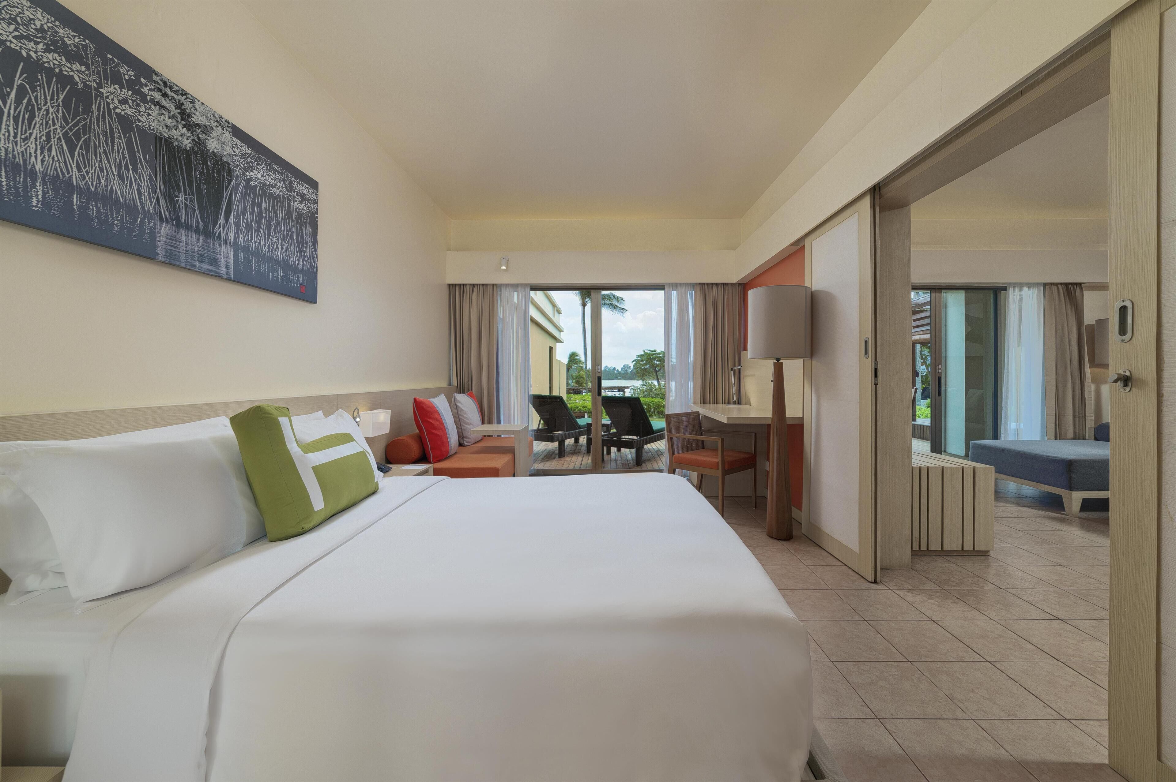 A hotel room with a large bed, a desk, a chair, and a view of the outdoors.