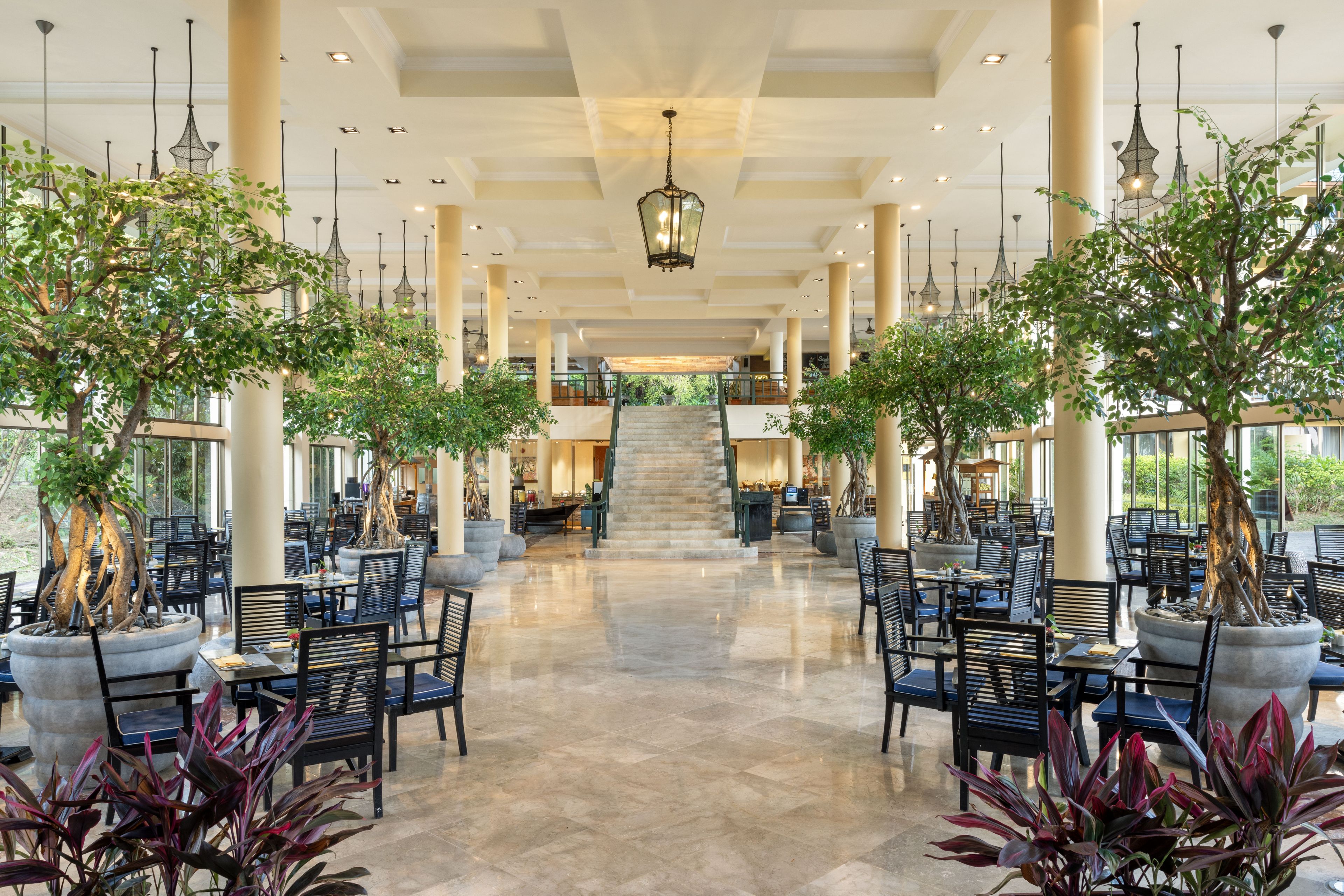 A spacious indoor area with multiple seating arrangements, a central staircase, and large windows allowing natural light.