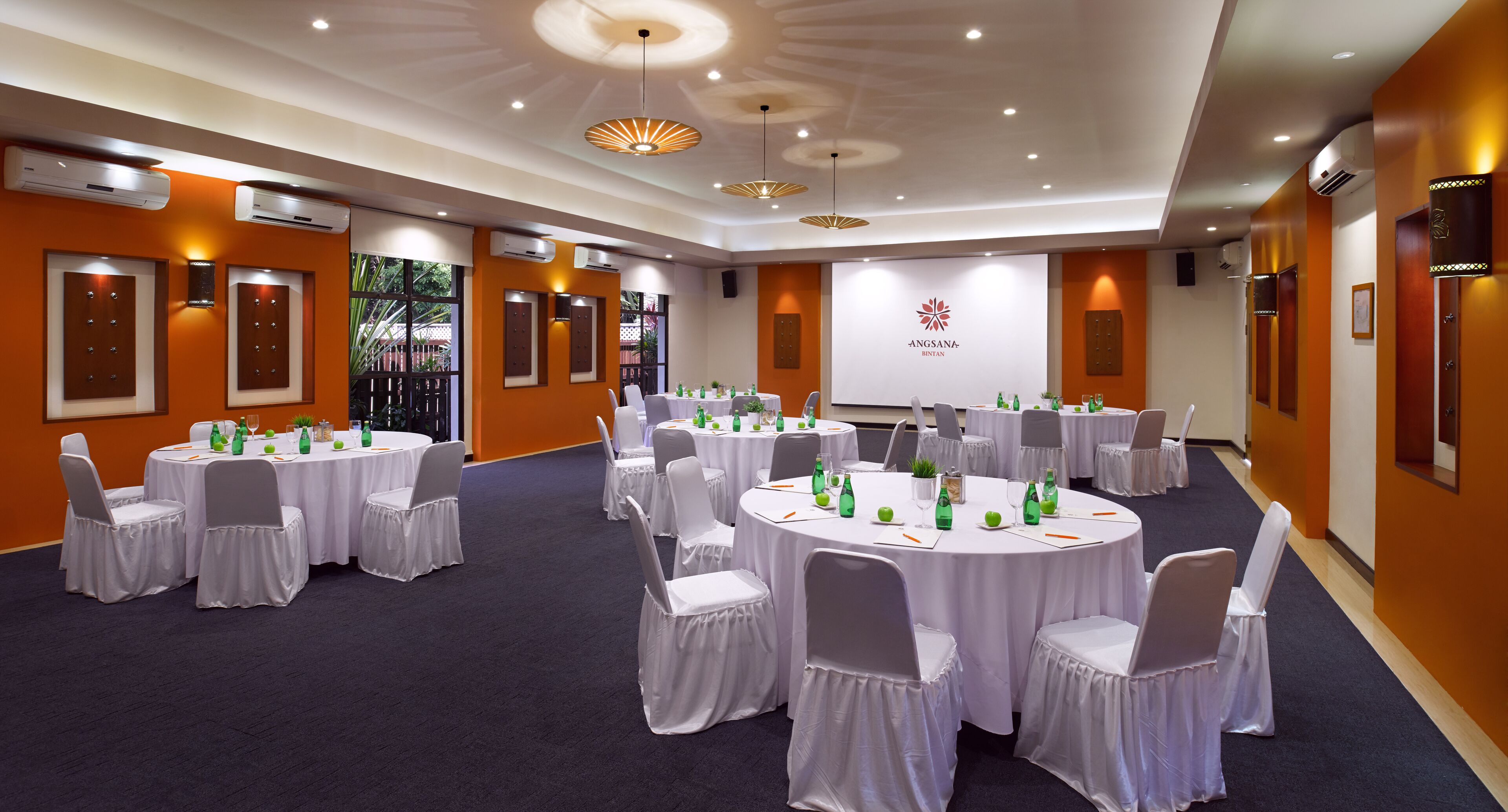 A conference room with multiple round tables, white chairs, and air conditioning units.
