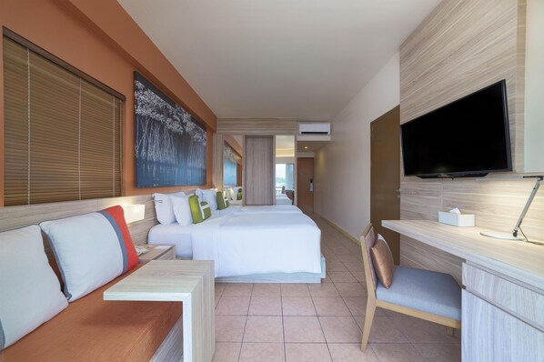 A hotel room with a large bed, a desk with a computer, a TV, and a window with blinds. - Homm Laguna Bintan (Bintan)