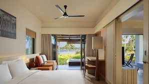 A hotel room with a bed, a desk, a chair, a ceiling fan, and a view of the beach. - Homm Laguna Bintan (Bintan)
