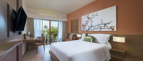 A hotel room with a large bed, a desk, a chair, a TV, and a window with a view of palm trees.