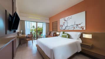 A hotel room with a large bed, a desk, a chair, a television, and a window with a view of palm trees.