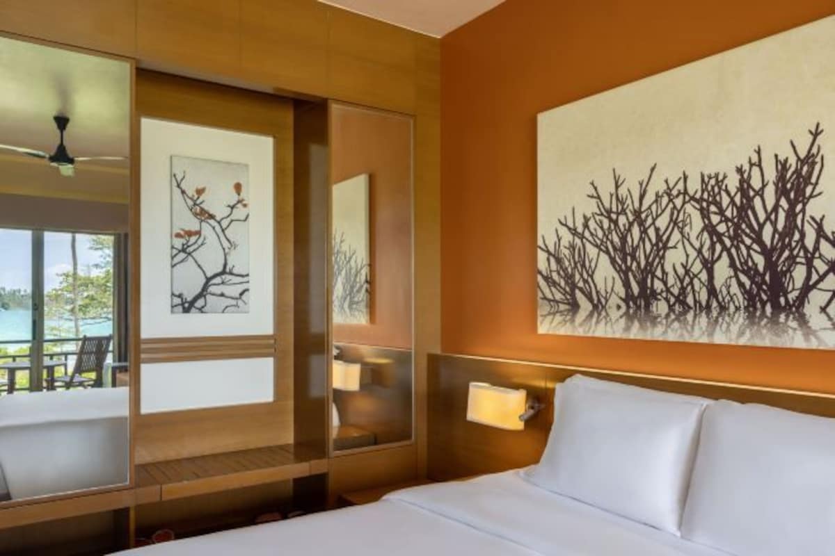 A hotel room with a bed, a large mirror, artwork on the wall, and a view of the outdoors.