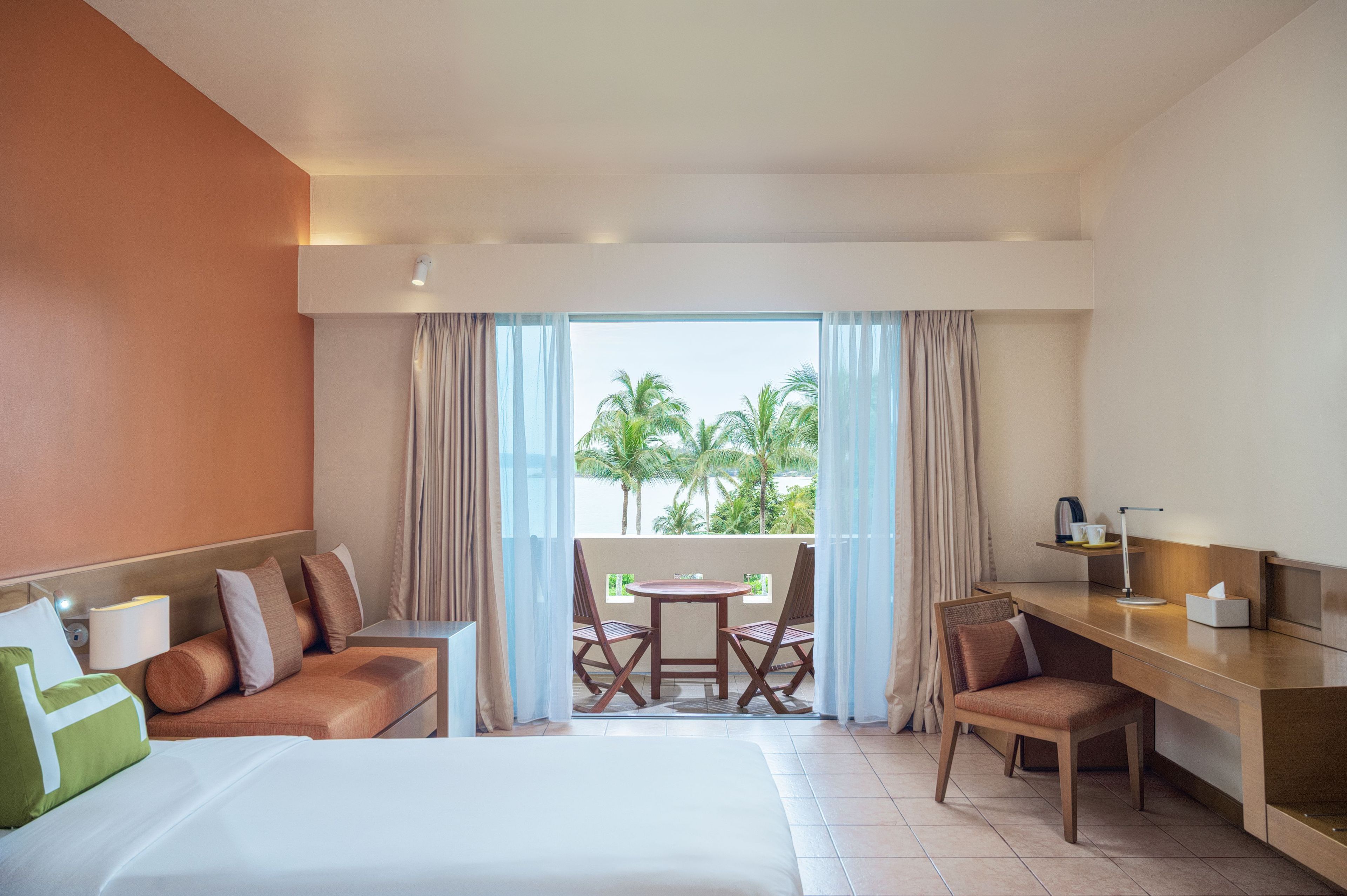 Une chambre d’hôtel comprenant un lit, un bureau, une chaise, une table et un balcon avec vue sur les palmiers.