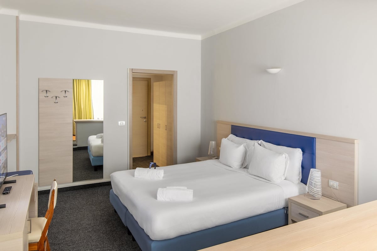A hotel room with a large bed, bedside tables, a desk, and a mirror.