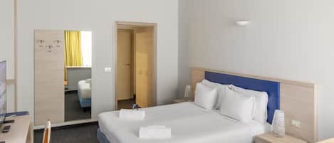 A hotel room with a large bed, bedside tables, a desk, and a mirror.